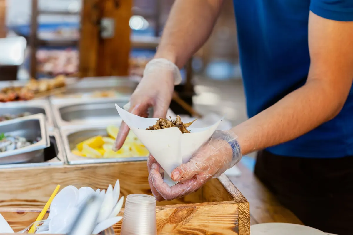 A vendor in gloves serving food from a market counter