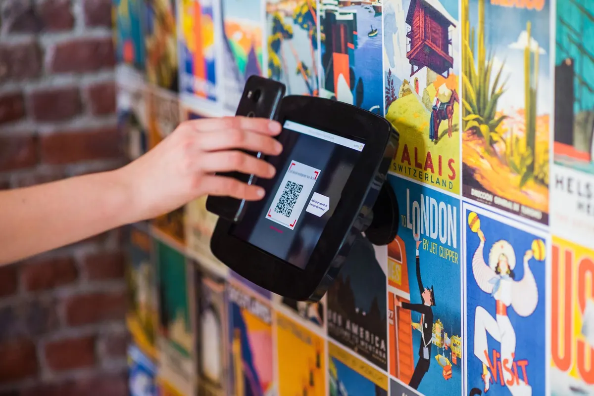 A phone screen being held up to a wall-mounted QR code scanner