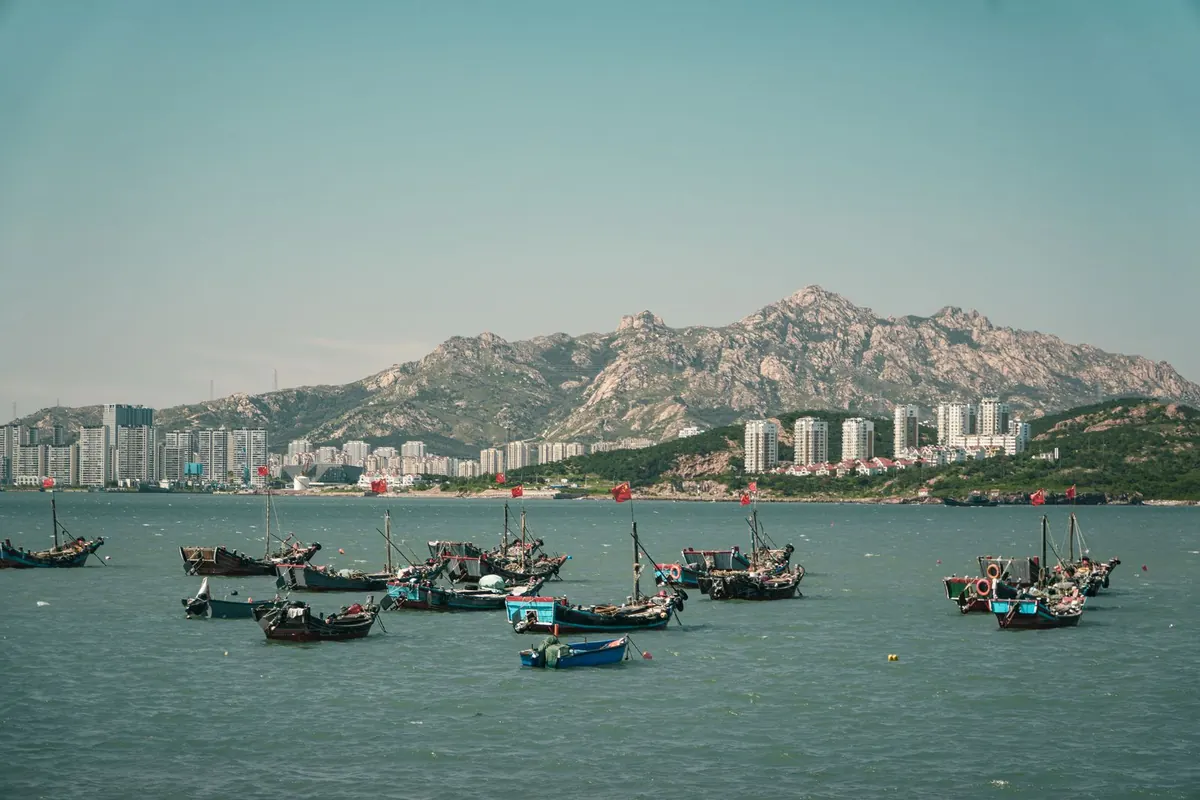 Fishing boats moored in a harbour below a mountain ridge.