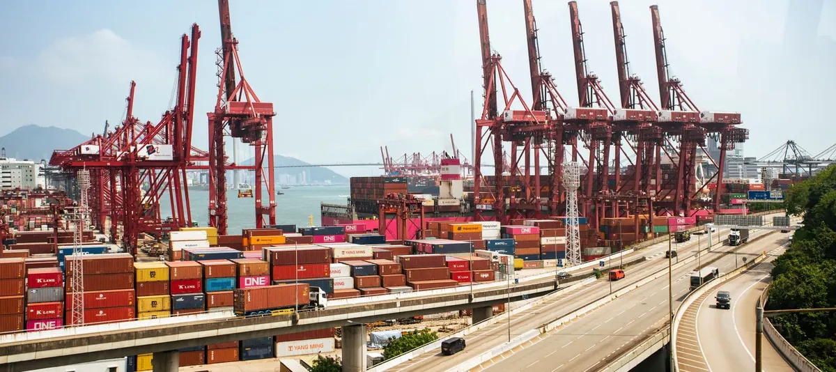 Red container cranes and stacked shipping containers at a working port.