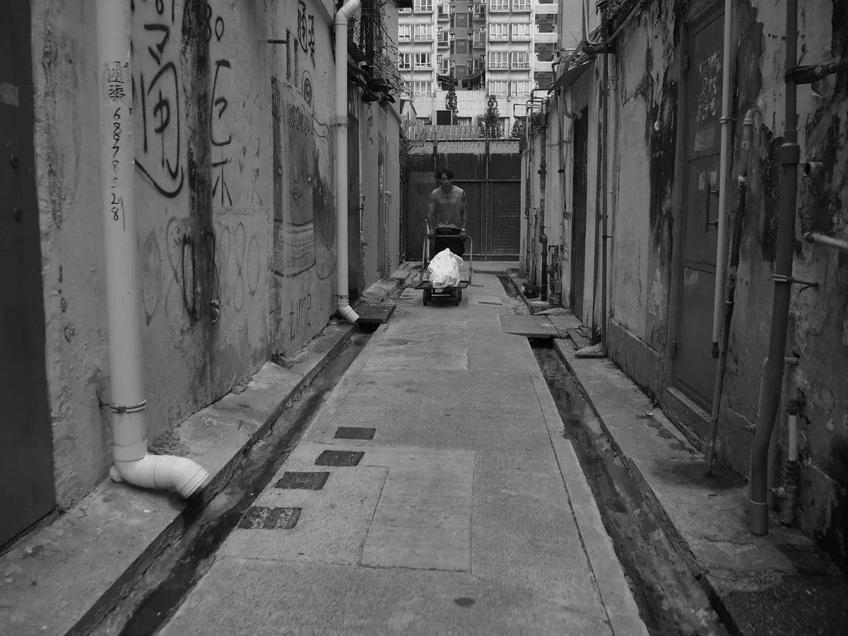 A narrow alley between tall residential buildings, in black and white.