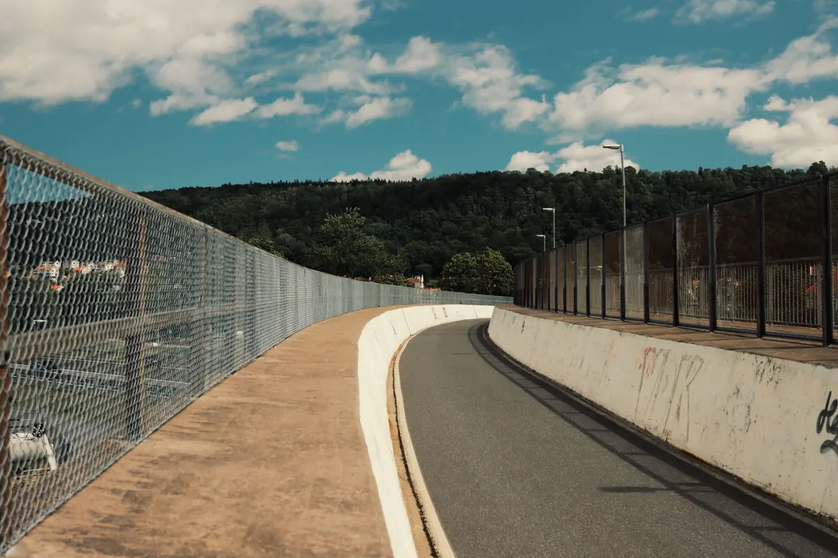 A narrow asphalt path running between a wire fence and trees.