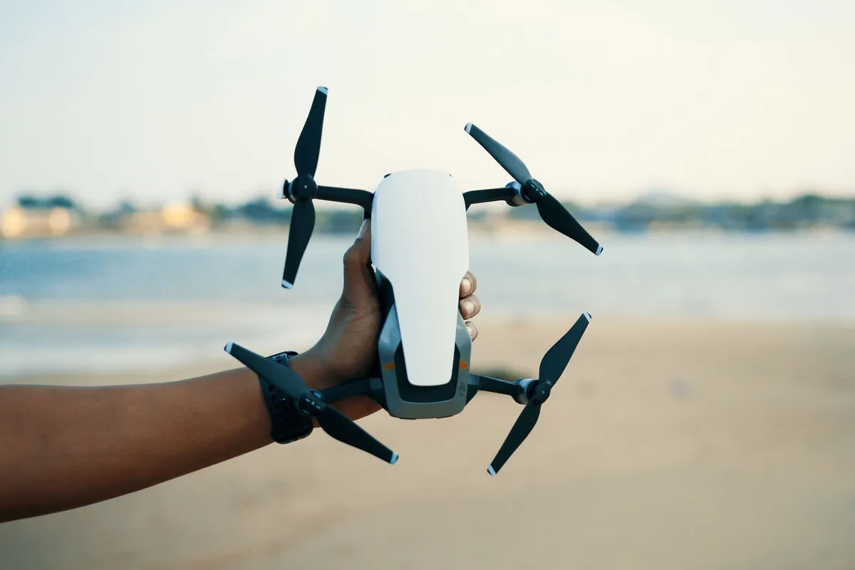 A hand holding a small white consumer drone.