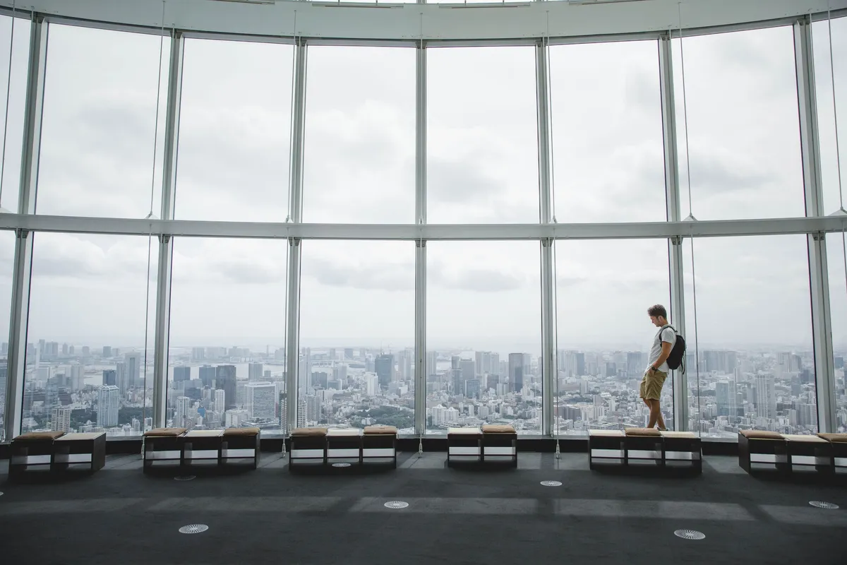 A man looking out over a city skyline from a high-rise observation window.