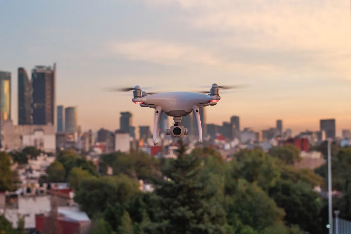 A white delivery drone flying above a city at sunset.