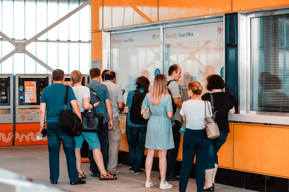 Stock photograph of people standing with their backs to the camera near a ticket office.