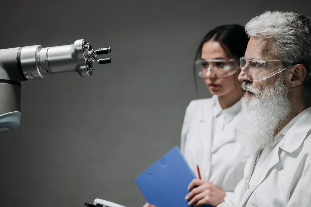 Stock photograph of two people in lab coats examining a robotic arm.
